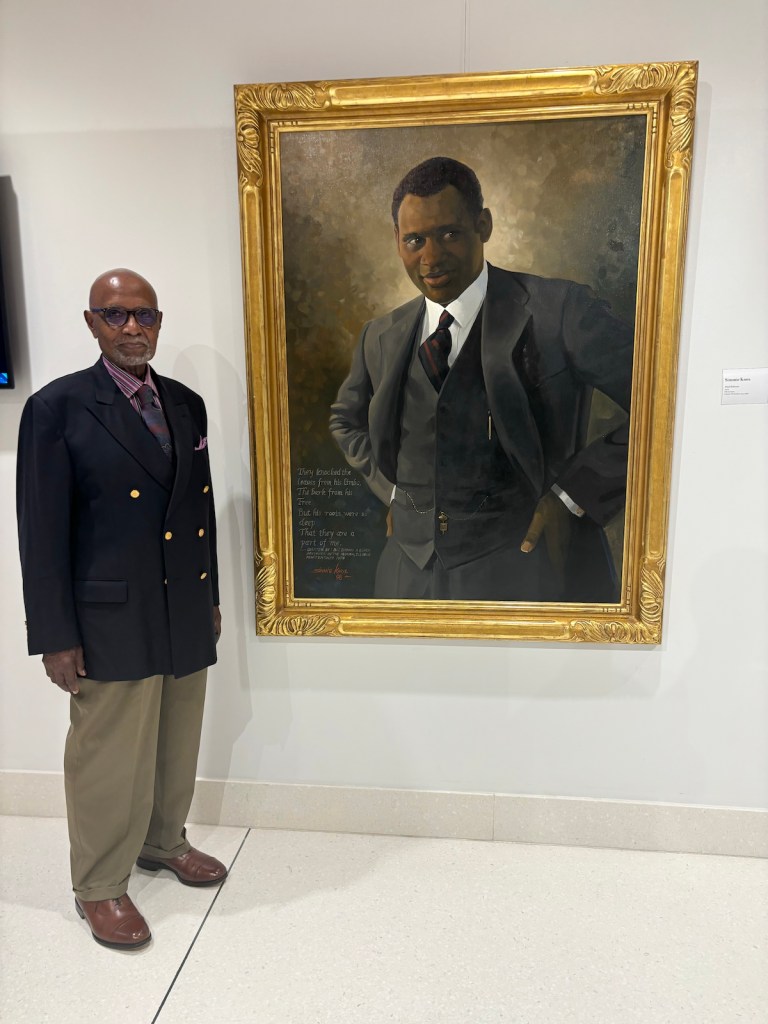 Celebrated artist Simmie Knox, the first African American to be commissioned for a presidential portrait, poses next to one of his multiple featured paintings, titled “Paul Robeson,” at Duke Ellington School of the Arts on Thursday, Sept. 12. (Jada Ingleton/The Washington Informer)