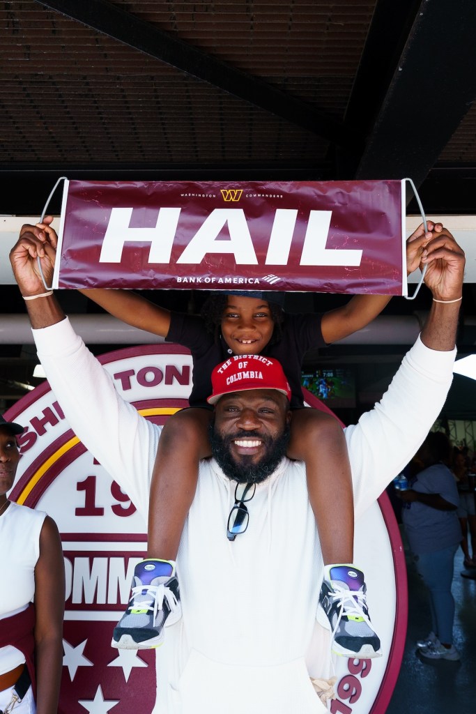 A dad holding the famous “Hail” Commanders poster with his son on his shoulders. (Marcus Relacion/The Washington Informer)