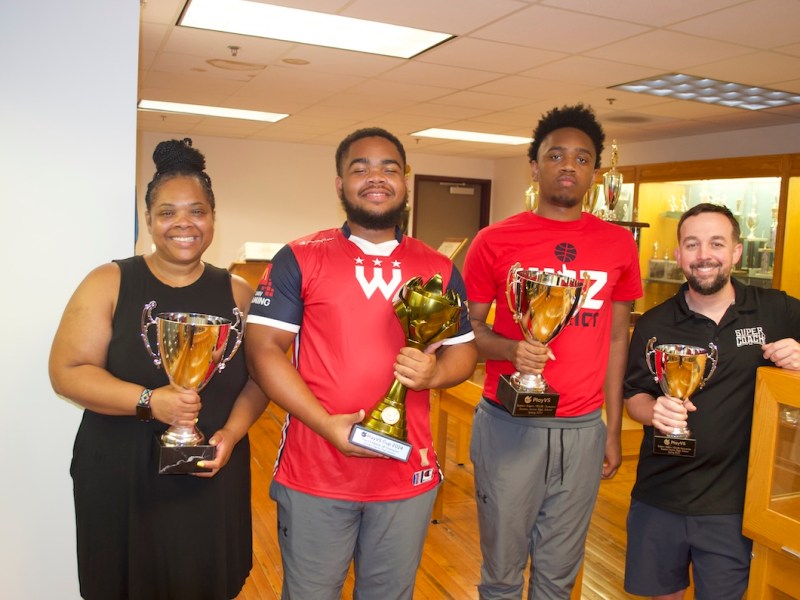 From left: Sherry Williams, Tyler Frost, Taylor Frost and coach Lee James pose with championship trophies in Eastern High's trophy room. (Demarco Rush/The Washington Informer)