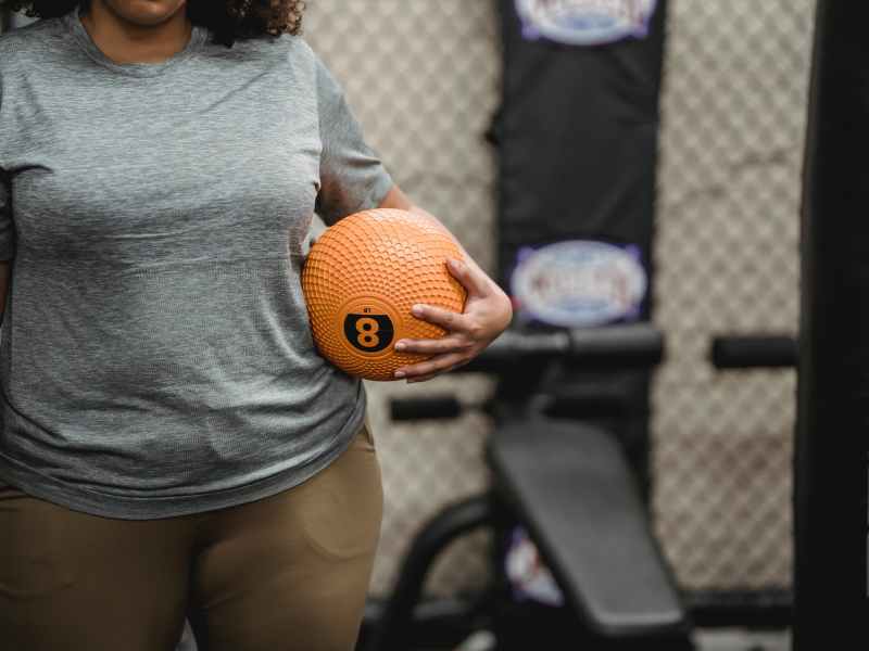 anonymous black woman with weight ball standing in modern gym