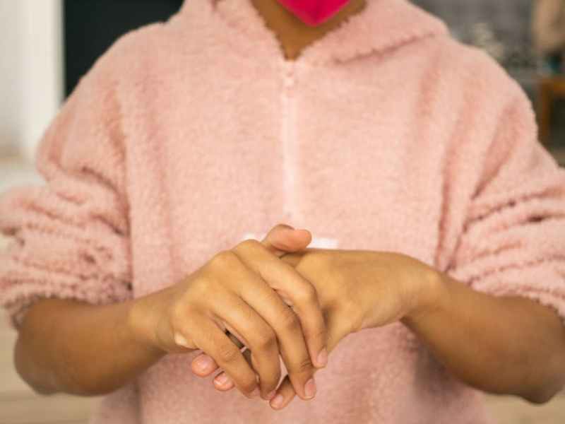 black girl in protective mask wiping hands with antiseptic